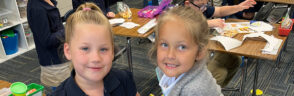 Two kindergarten girls smiling and sitting at their desks looking at the camera